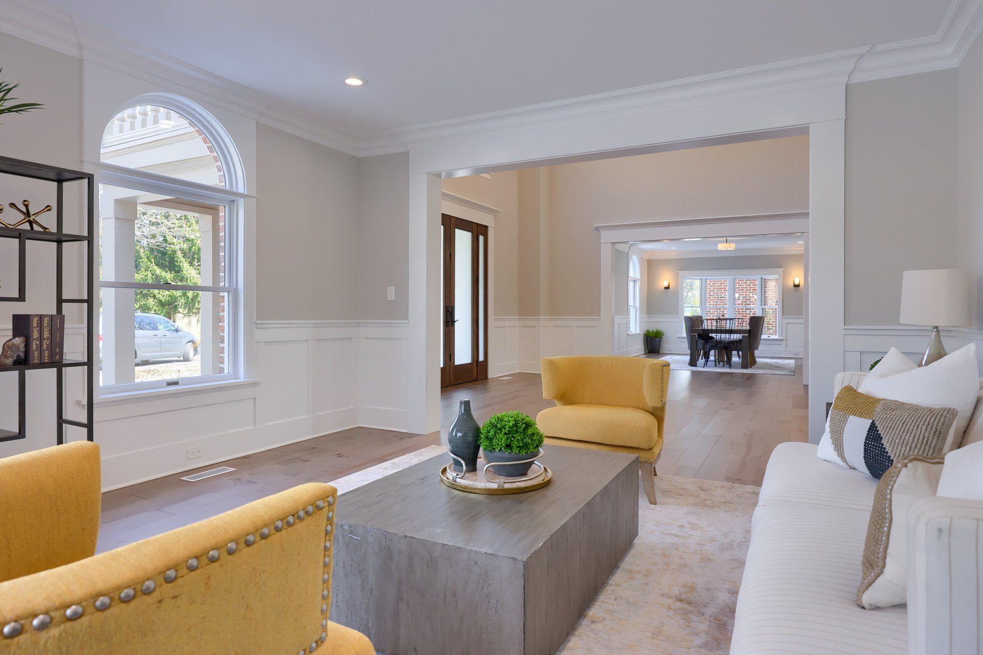 Bright, airy living room with yellow chairs, white sofa, and a long gray coffee table leading to a dining area.
