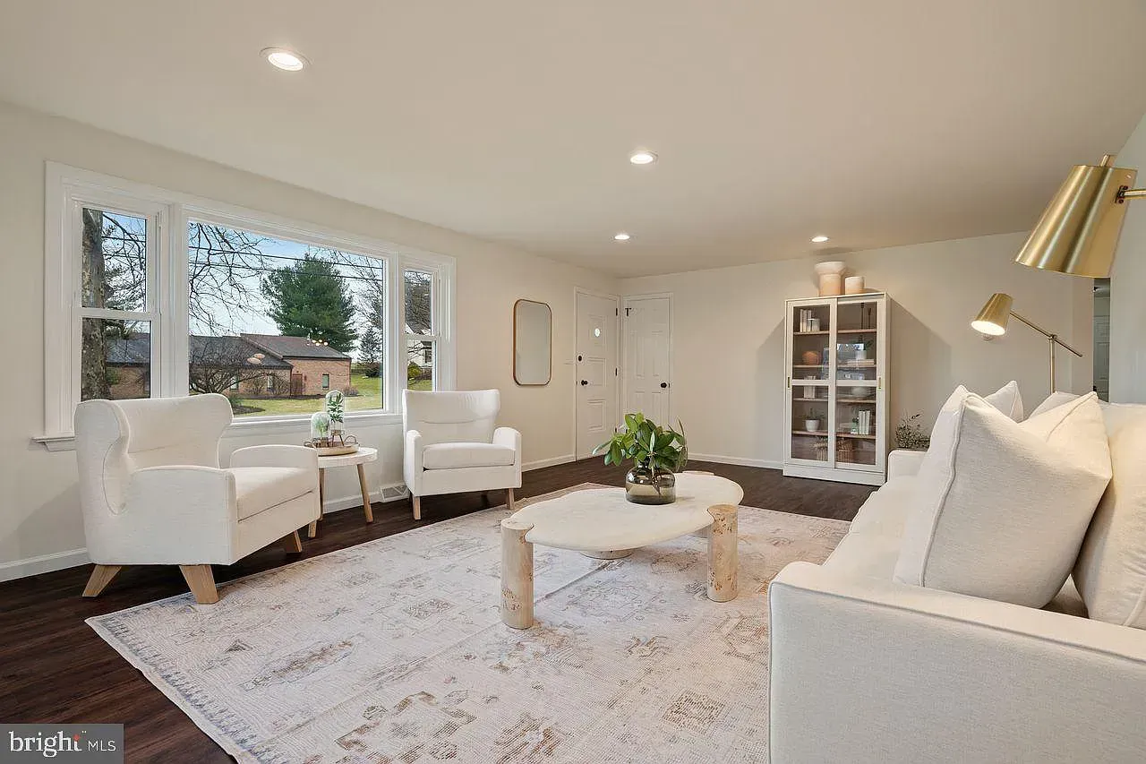 Bright modern living room with white furniture, shag rug, coffee table, and large windows