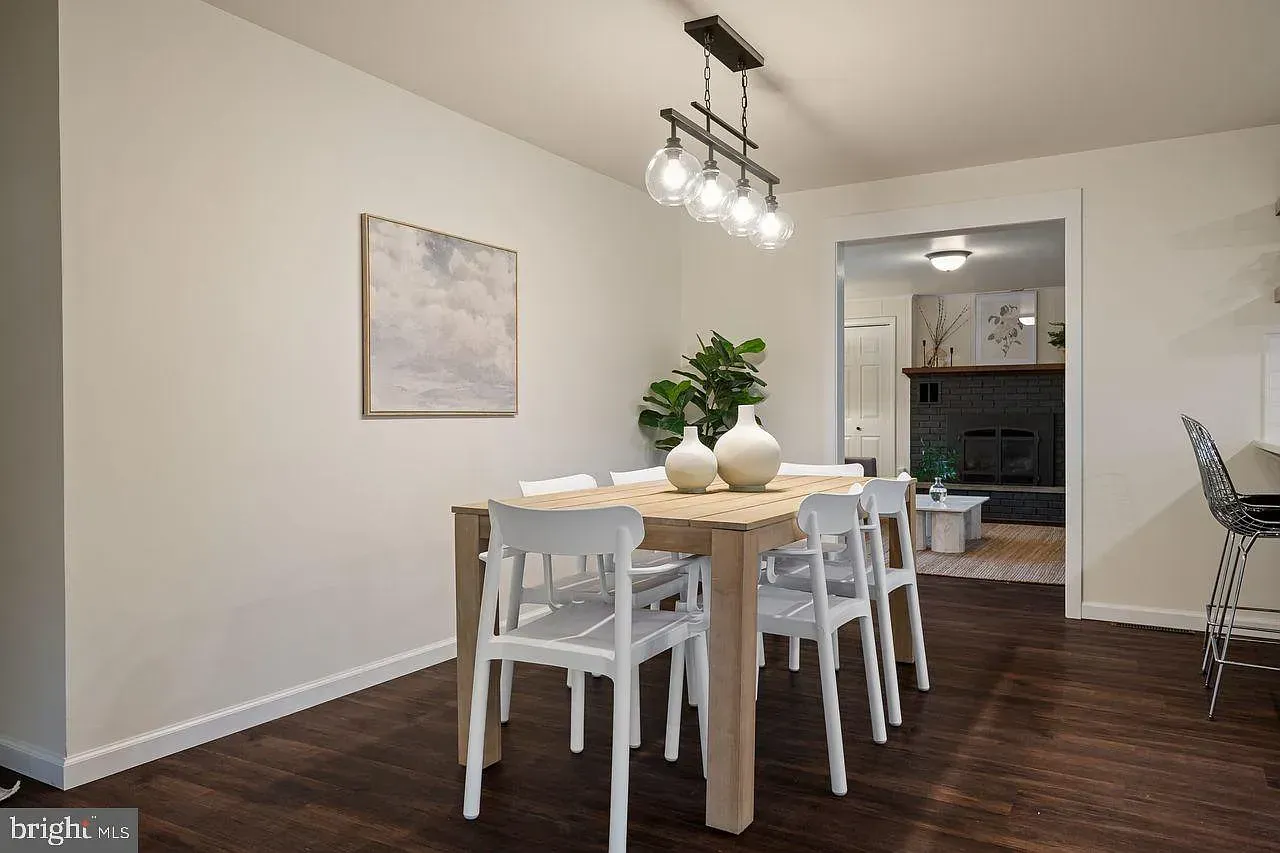 Dining room with a wooden table, white chairs, wall art, and a chandelier leading into a kitchen.