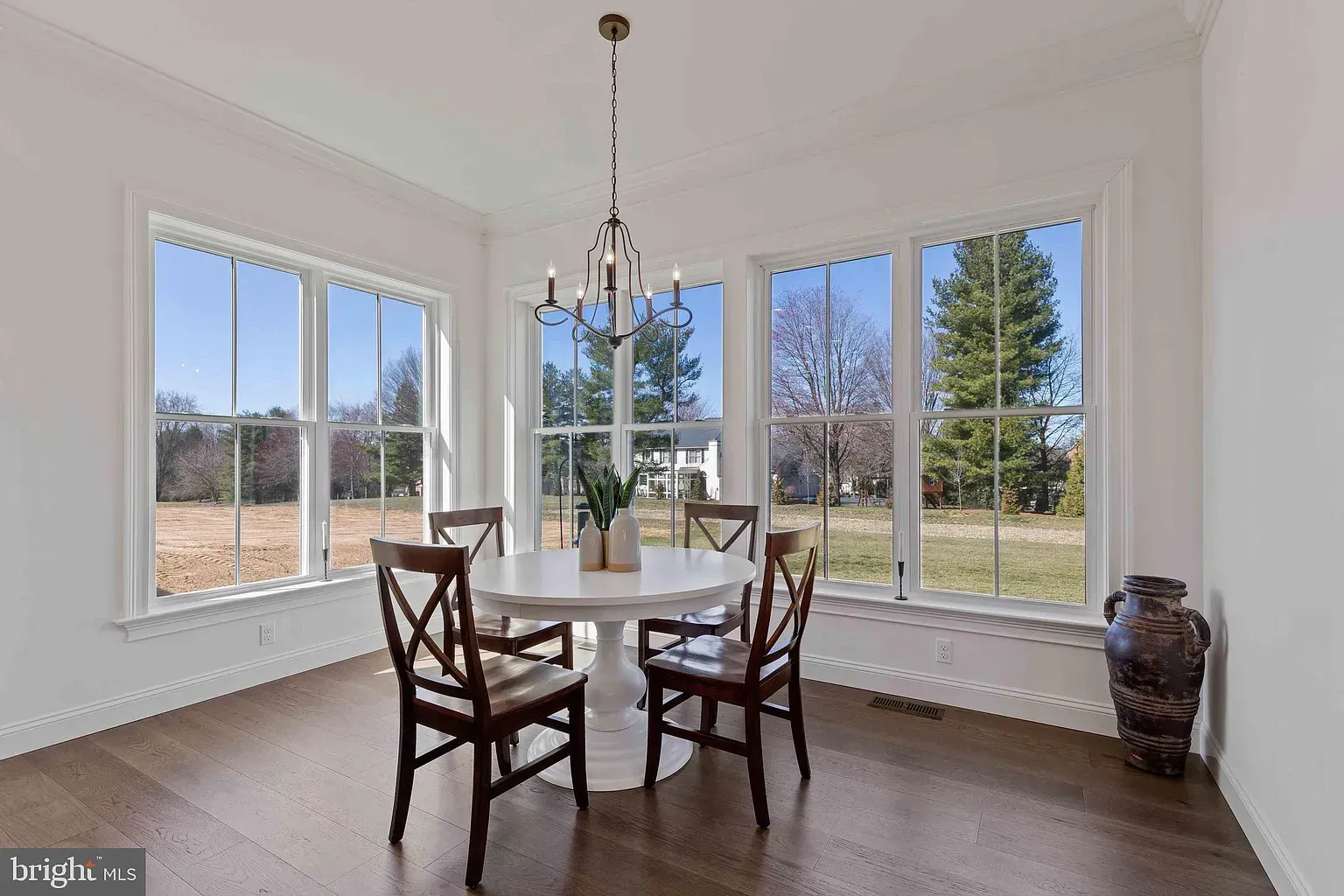 Bright dining room with large windows, a round table, four chairs, and a hanging light fixture