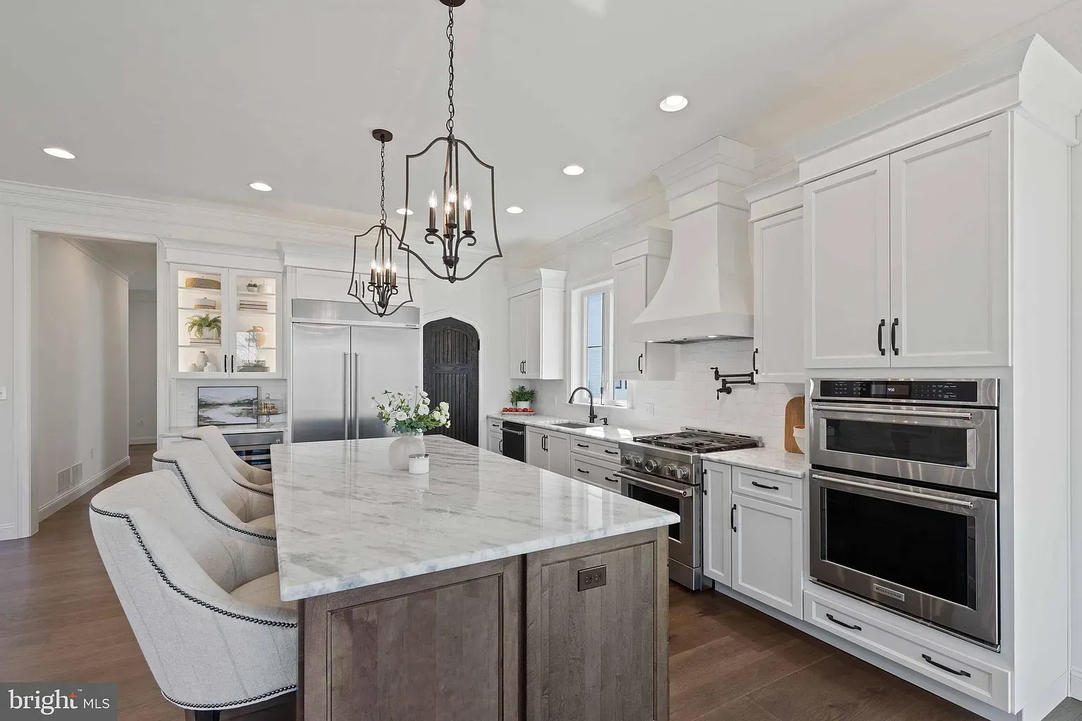 Bright white modern kitchen with large marble island, pendant lights, and stainless steel appliances