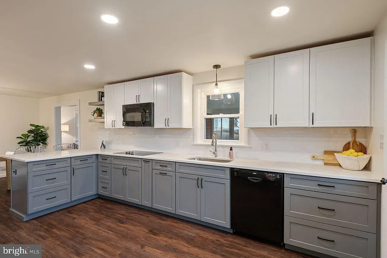 Bright modern kitchen with gray and white cabinets, white counters, dark wood floor, and black appliances