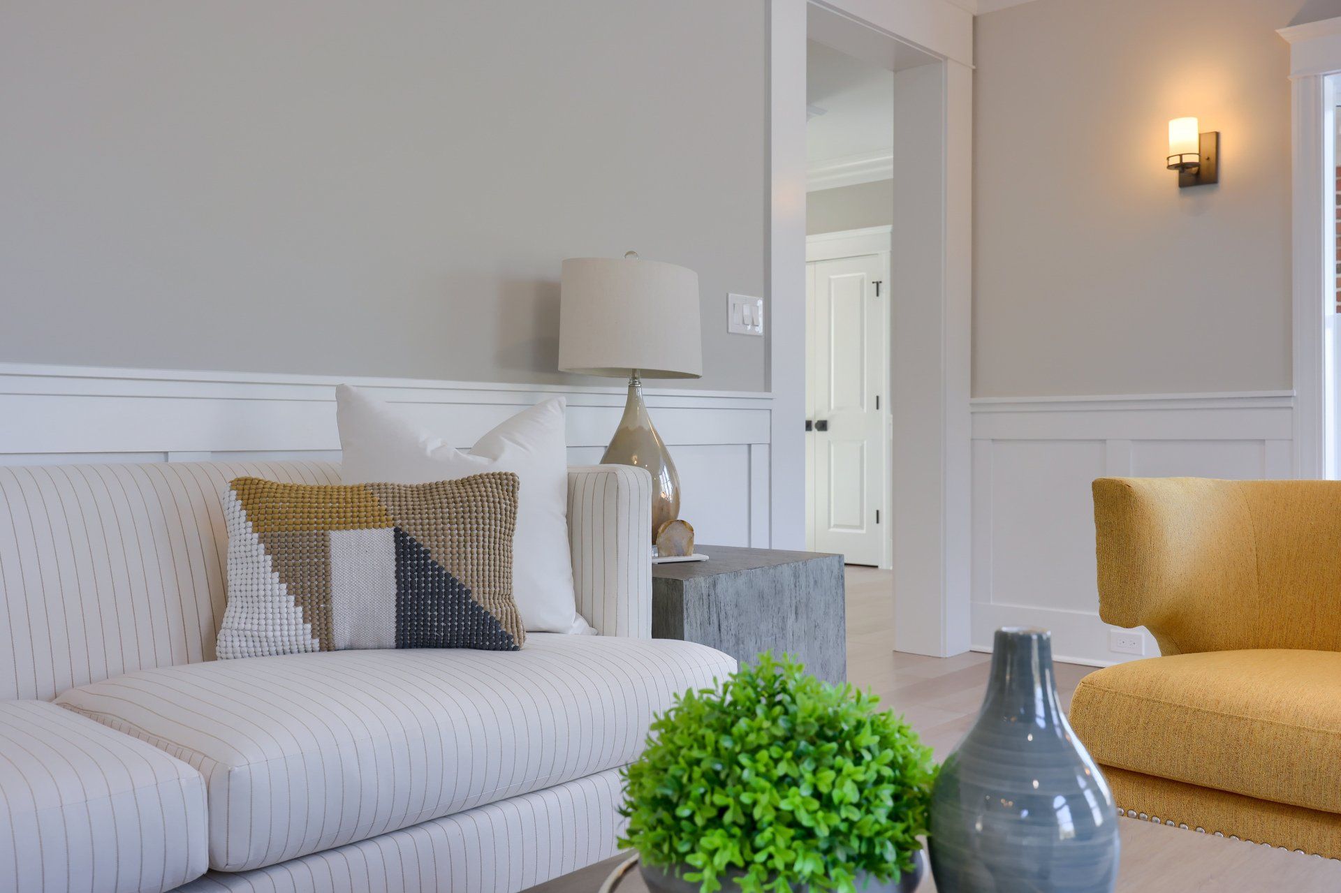 Bright living room with white sofa, yellow armchair, gray lamp, and green plant