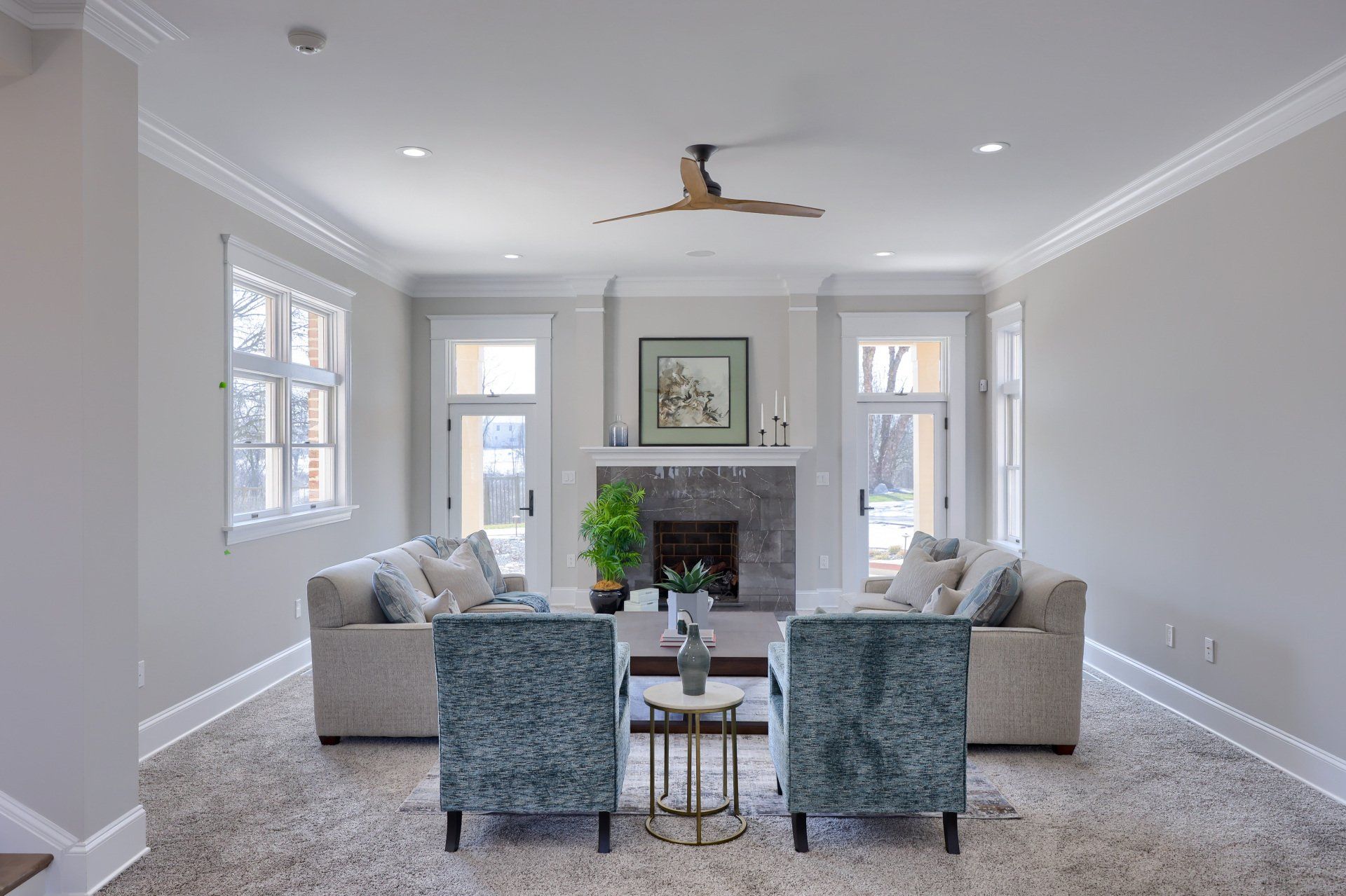 Bright living room with gray sofas, patterned chairs, fireplace, and large windows