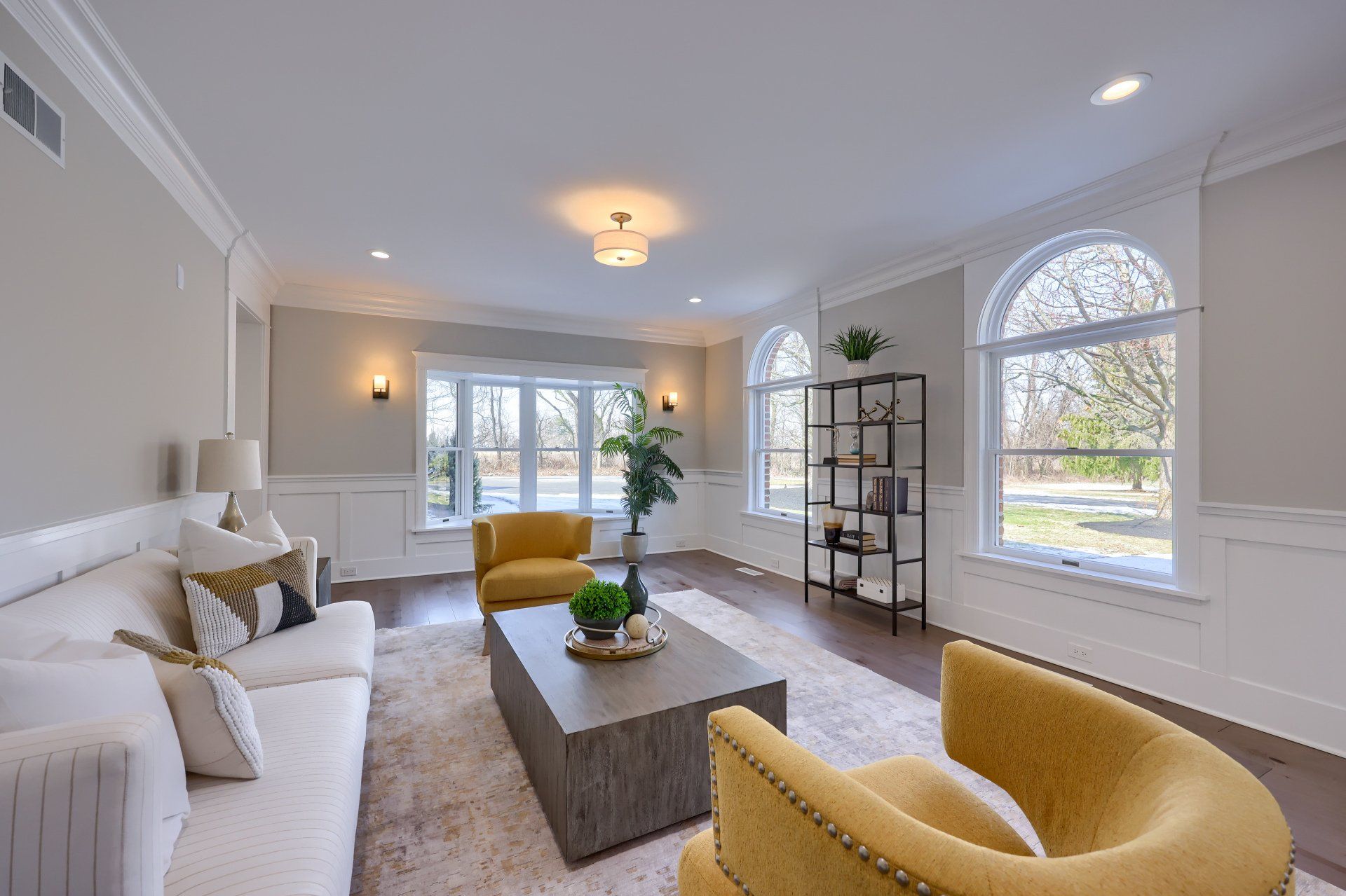 Bright, modern living room with white sofa, mustard chairs, coffee table, and large arched window