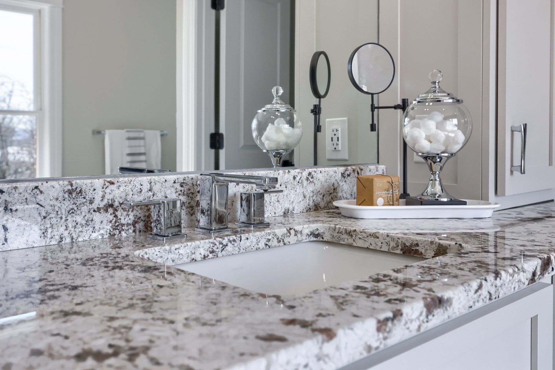 Modern bathroom vanity with speckled granite countertop, mirror, and decorative jars and candles