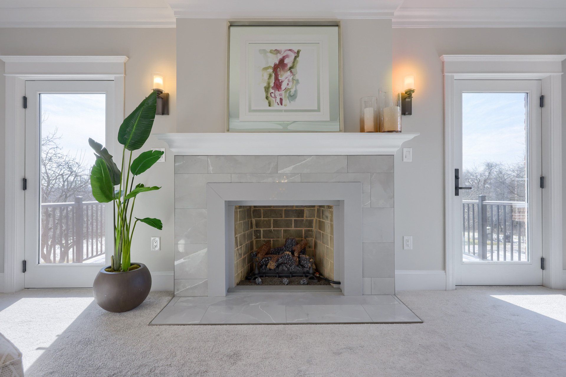 Bright living room with white fireplace, framed art, twin windows, and a potted plant.
