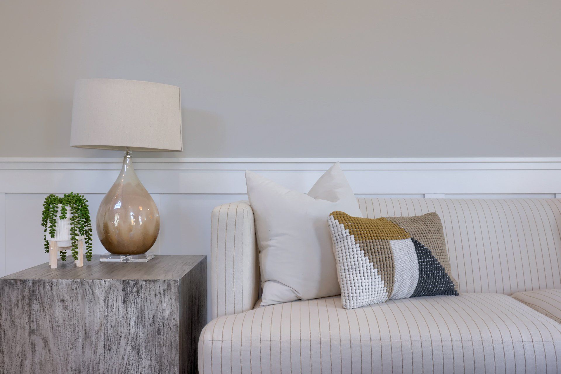 Minimal living room with striped sofa, gold lamp, gray side table, and white pillows.