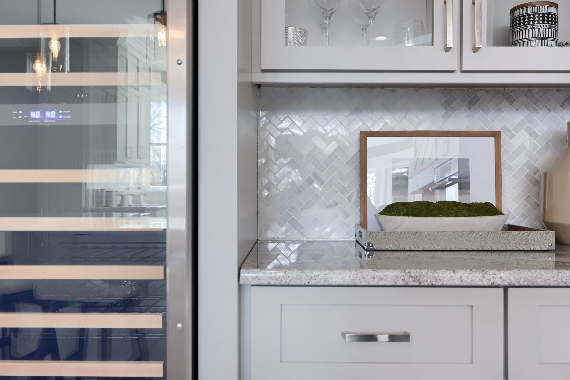 Modern kitchen with white cabinets, granite countertop, herringbone backsplash, and glass door on the left