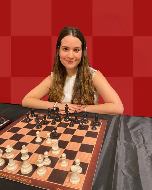 A woman is sitting at a table with a chess board.
