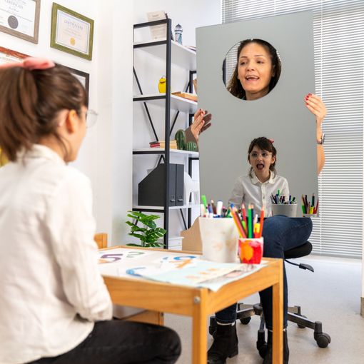 Female speech pathologist holding out a mirror in front of young girl patient