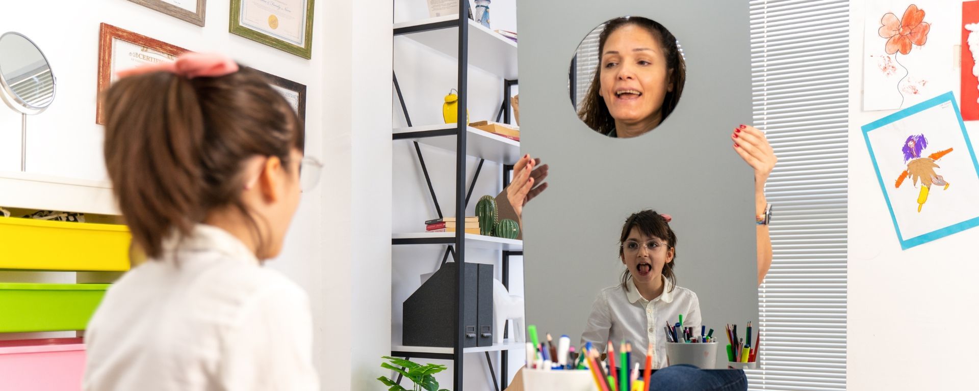 Female speech pathologist holding up mirror in front of young female patient
