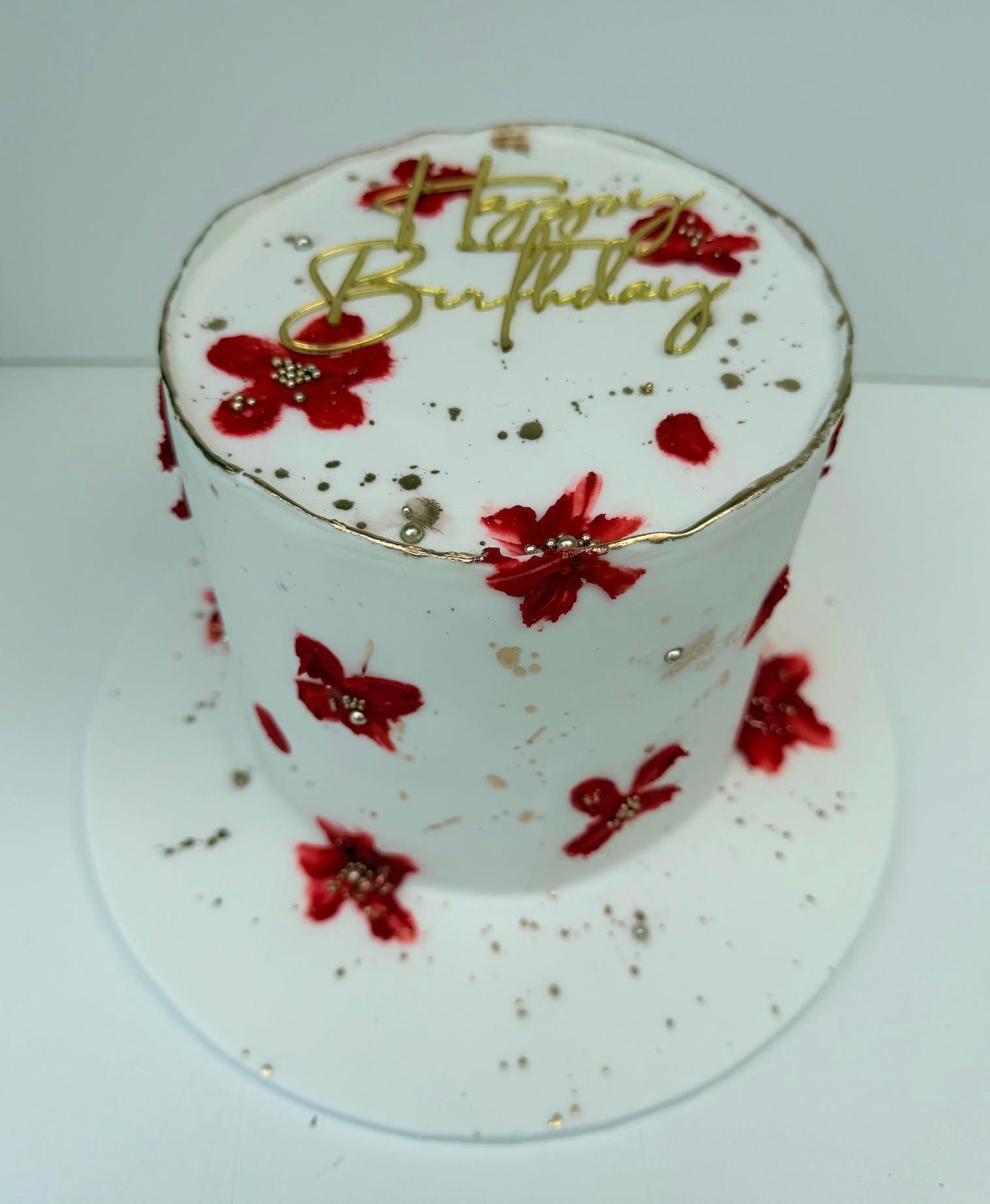 White birthday cake adorned with red floral patterns and gold