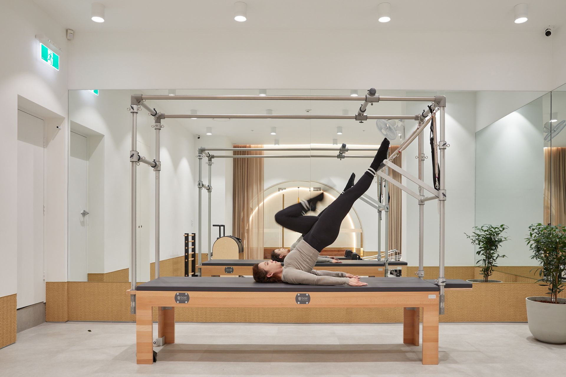 Person performing a Pilates leg lift on a reformer in a bright studio