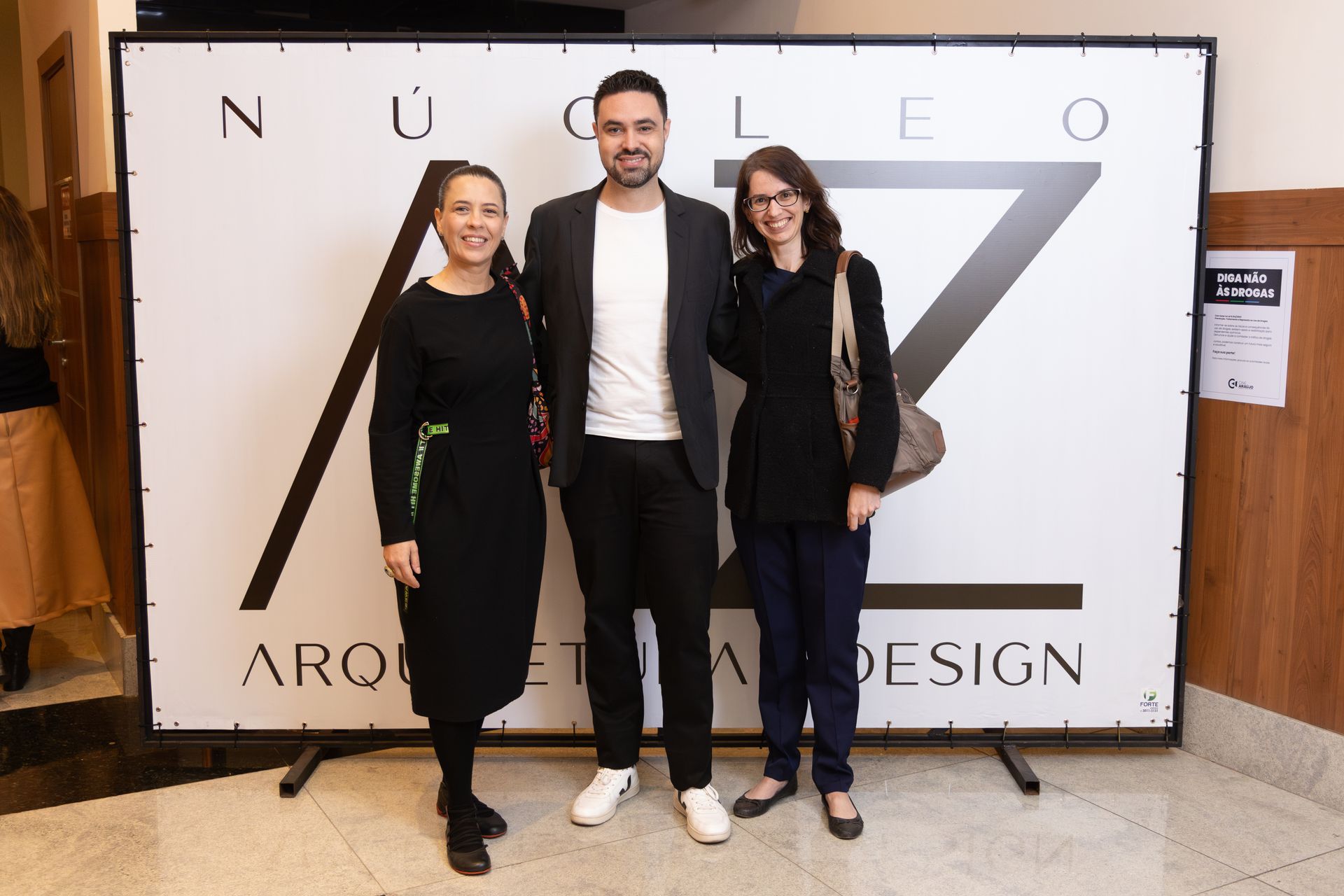 Um homem e duas mulheres estão posando para uma foto em frente a uma placa que diz design.