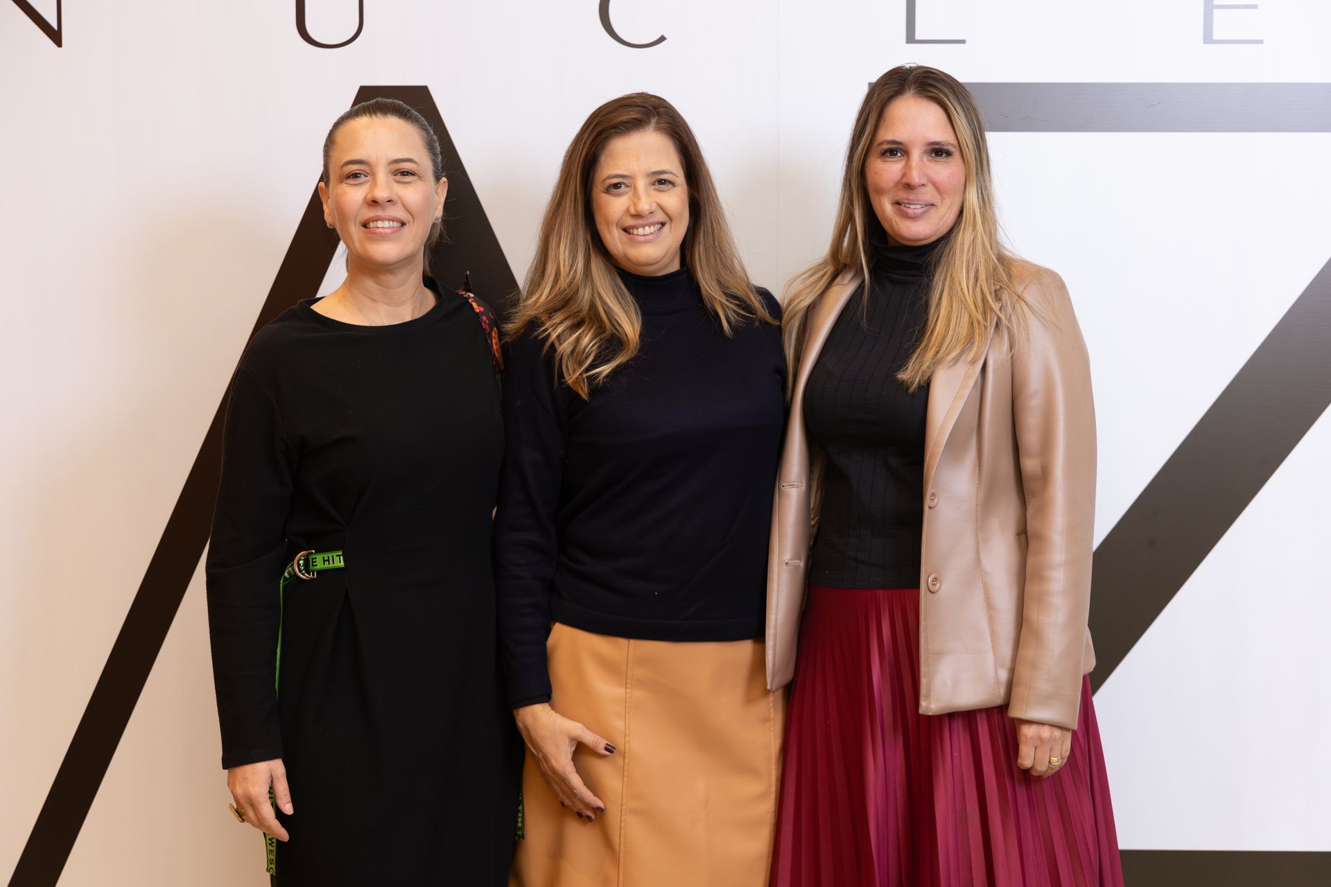 Três mulheres estão posando para uma foto em frente a uma parede.