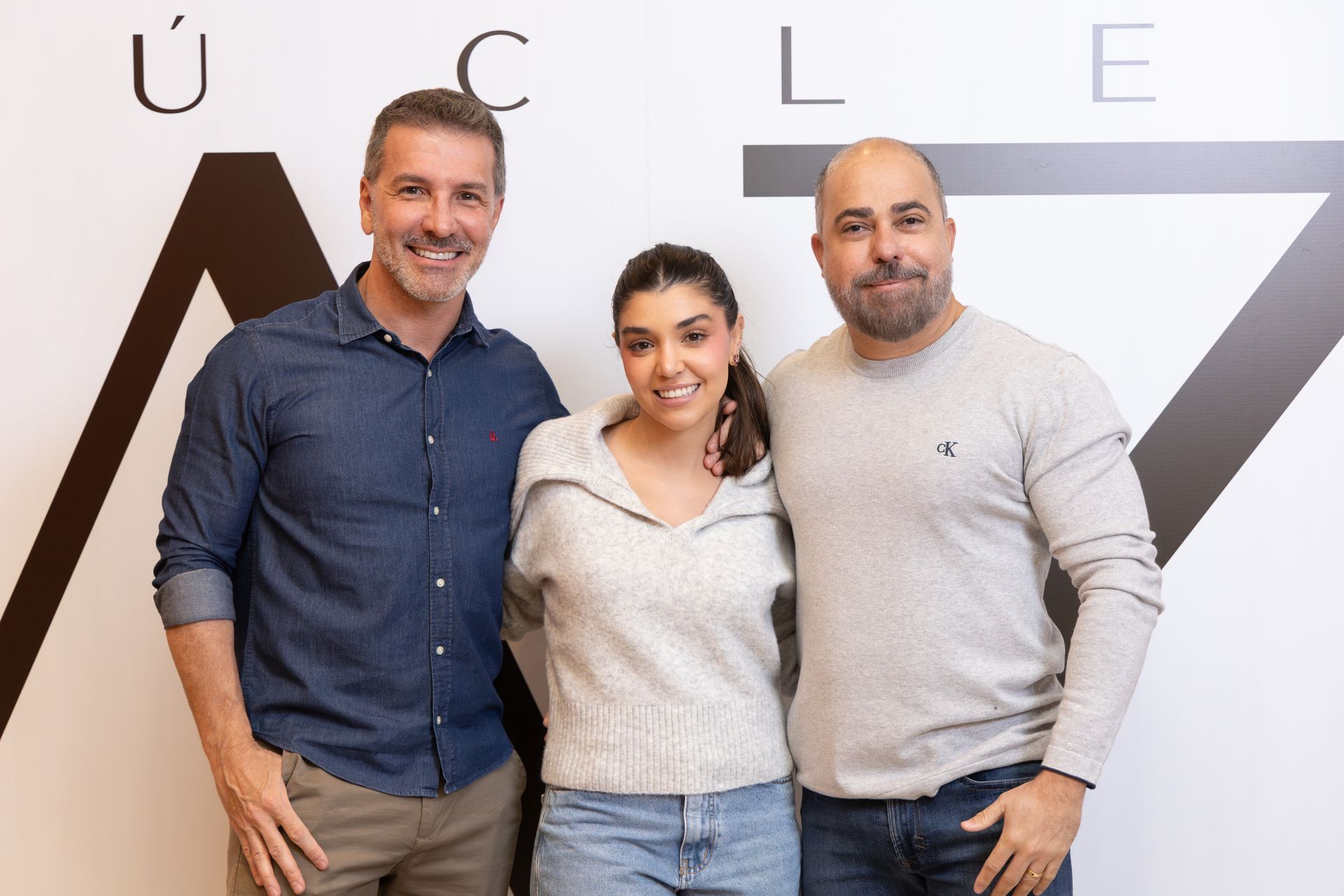 Três pessoas estão posando para uma foto em frente a uma parede com as letras ucl nela.