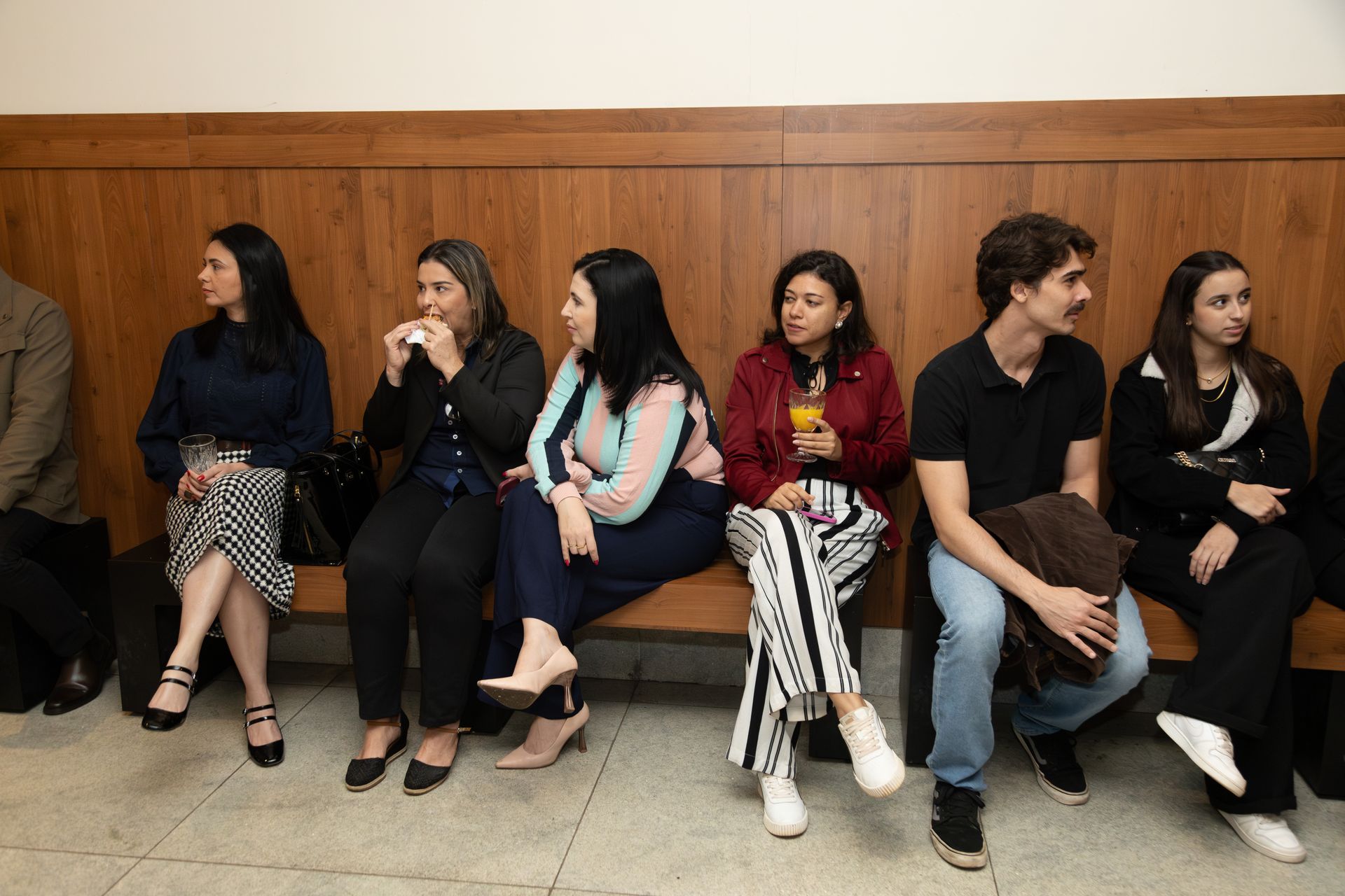 Um grupo de pessoas está sentado em um banco em uma sala.
