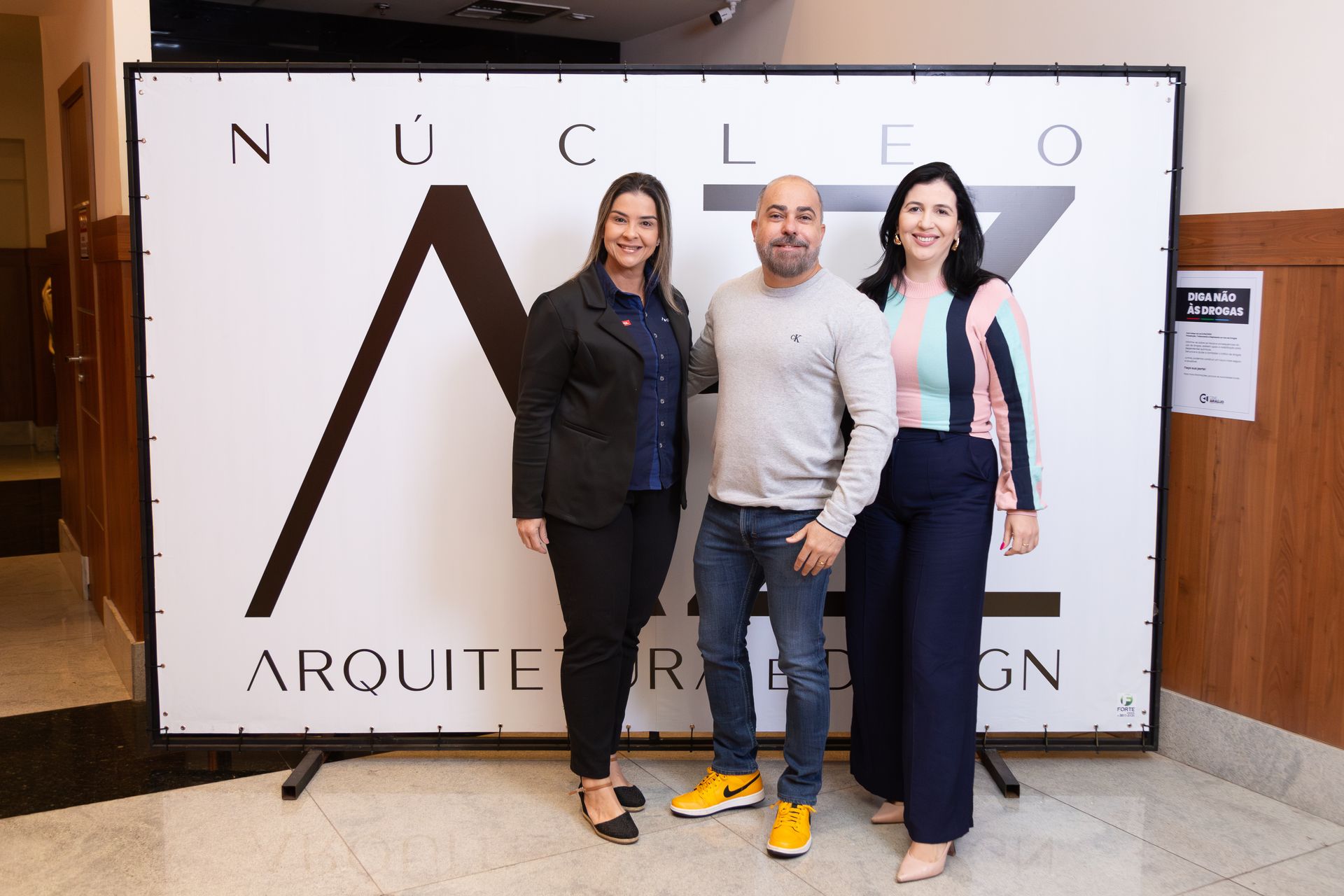 Três pessoas estão posando para uma foto em frente a uma placa que diz nucleo
