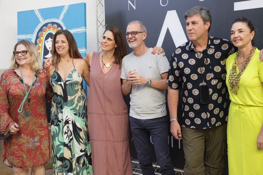 Um grupo de pessoas em pé, uma ao lado da outra, em frente a uma parede.