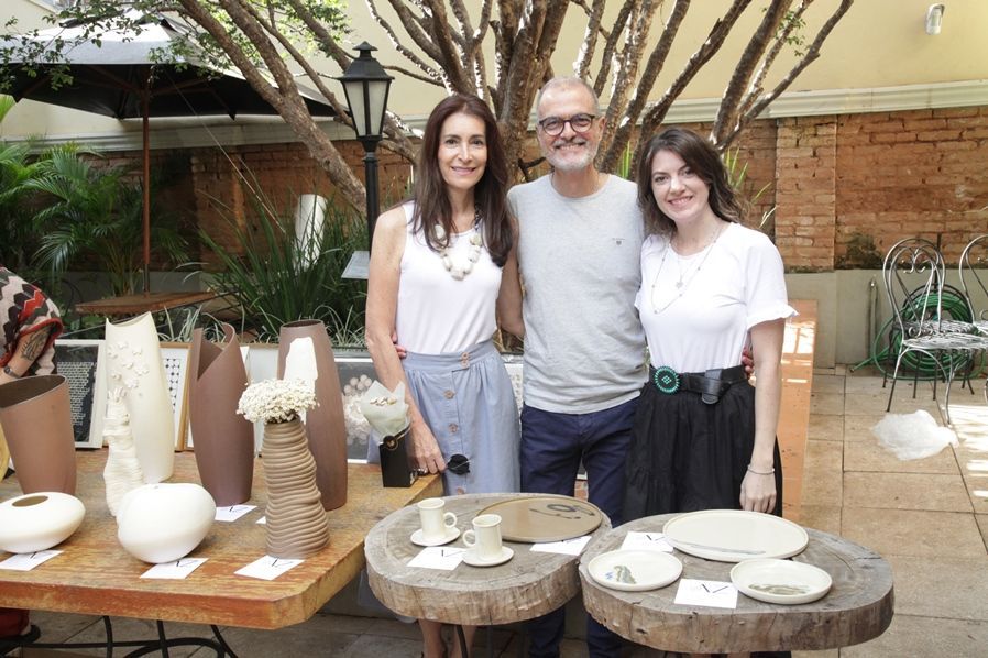 Um homem e duas mulheres estão posando para uma foto em frente a uma mesa com vasos sobre ela.