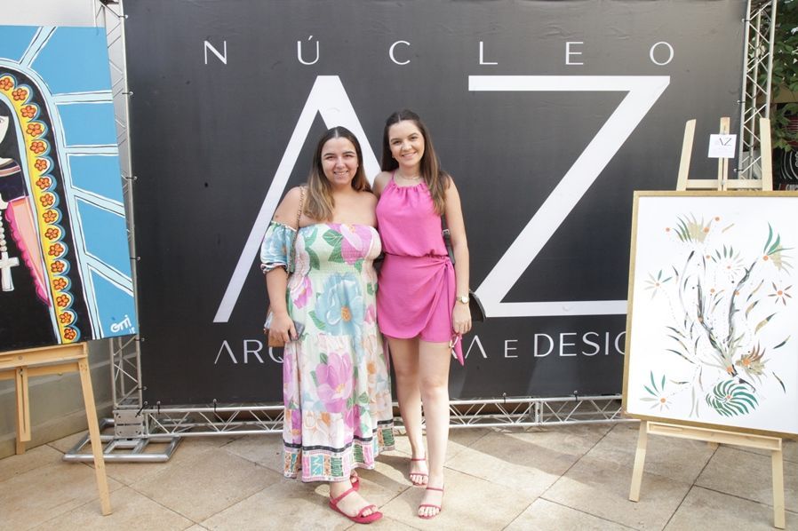 Duas mulheres posam para uma foto em frente a uma placa que diz nucleo