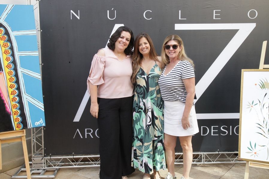 Três mulheres estão posando para uma foto em frente a uma placa que diz nucleo