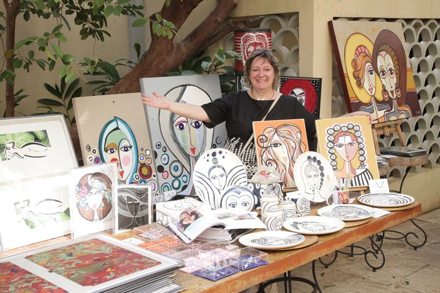 Uma mulher está parada em frente a uma mesa com pratos e pinturas sobre ela.