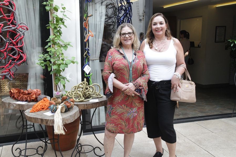 Duas mulheres estão de pé, uma ao lado da outra, em frente a uma loja.
