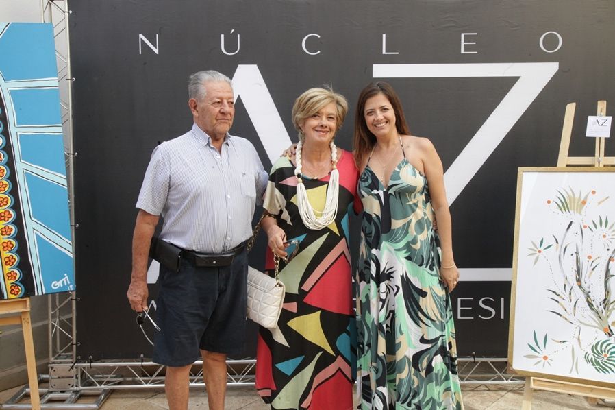 Três pessoas estão posando para uma foto em frente a uma placa que diz nucleo