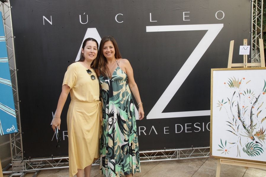 Duas mulheres posam para uma foto em frente a uma placa que diz nucleo