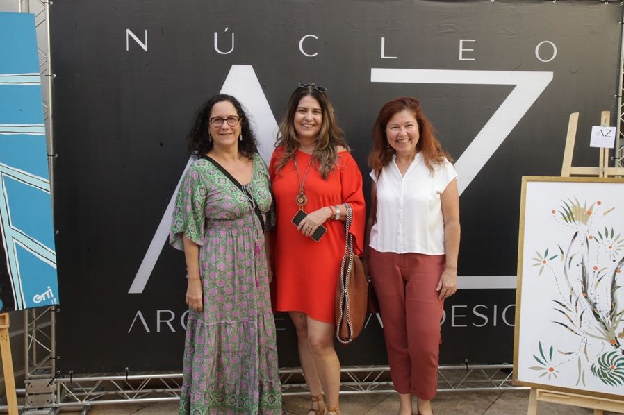Três mulheres estão posando para uma foto em frente a uma placa que diz nucleo