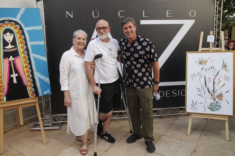Três pessoas em pé na frente de uma placa que diz nucleo