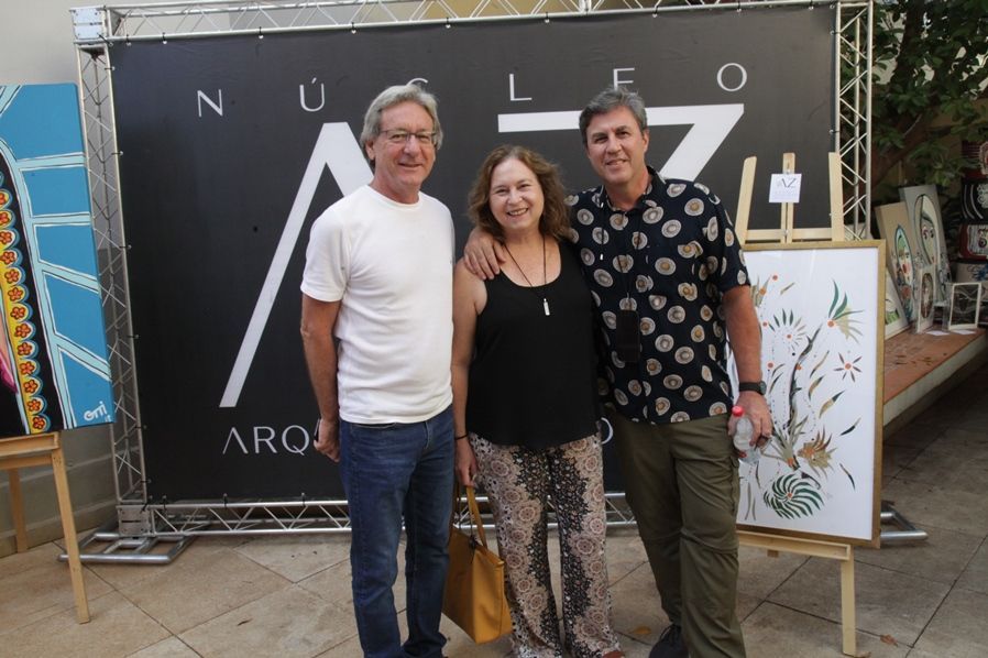 Três pessoas estão posando para uma foto em frente a uma placa que diz nucleo