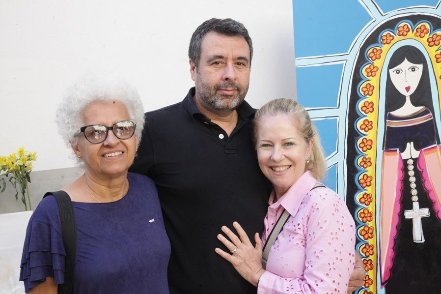 Um homem e duas mulheres estão posando para uma foto em frente a uma pintura.