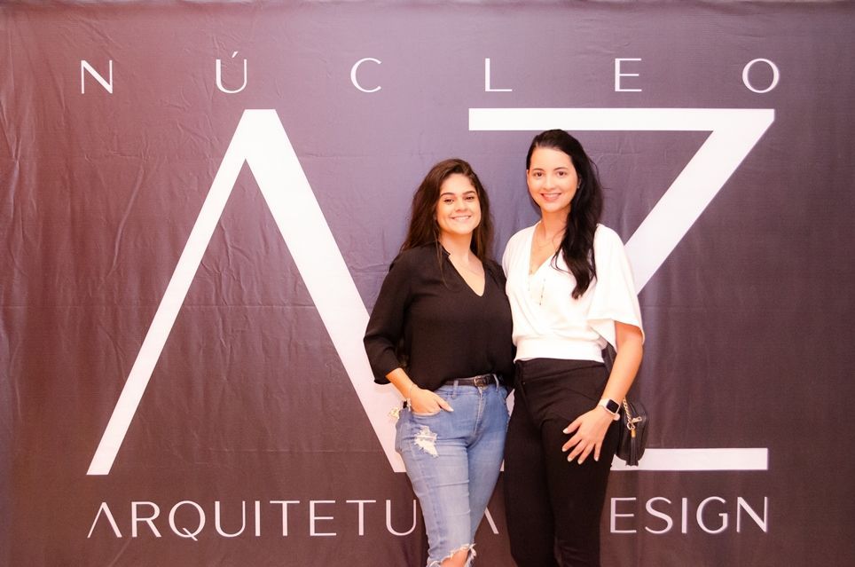 Duas mulheres posam para uma foto em frente a uma placa que diz nucleo