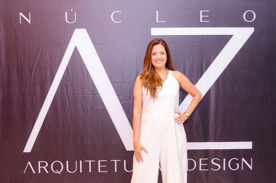 Uma mulher de macacão branco está em frente a uma placa que diz nucleo arquiteto design