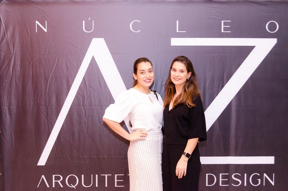 Duas mulheres estão posando para uma foto em frente a uma placa que diz nucleo arquite design.