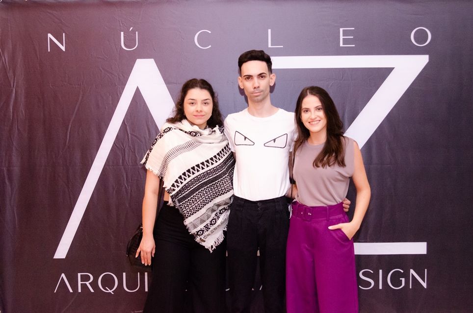Três pessoas estão posando para uma foto em frente a uma placa que diz nucleo arqui