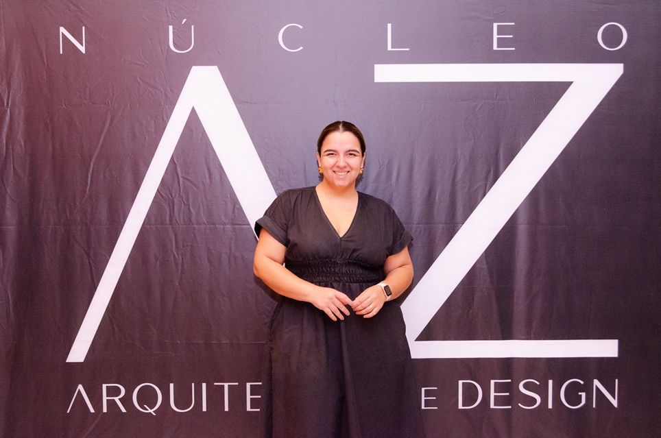 Uma mulher de vestido preto está em frente a uma placa que diz nucleo arquitete e design