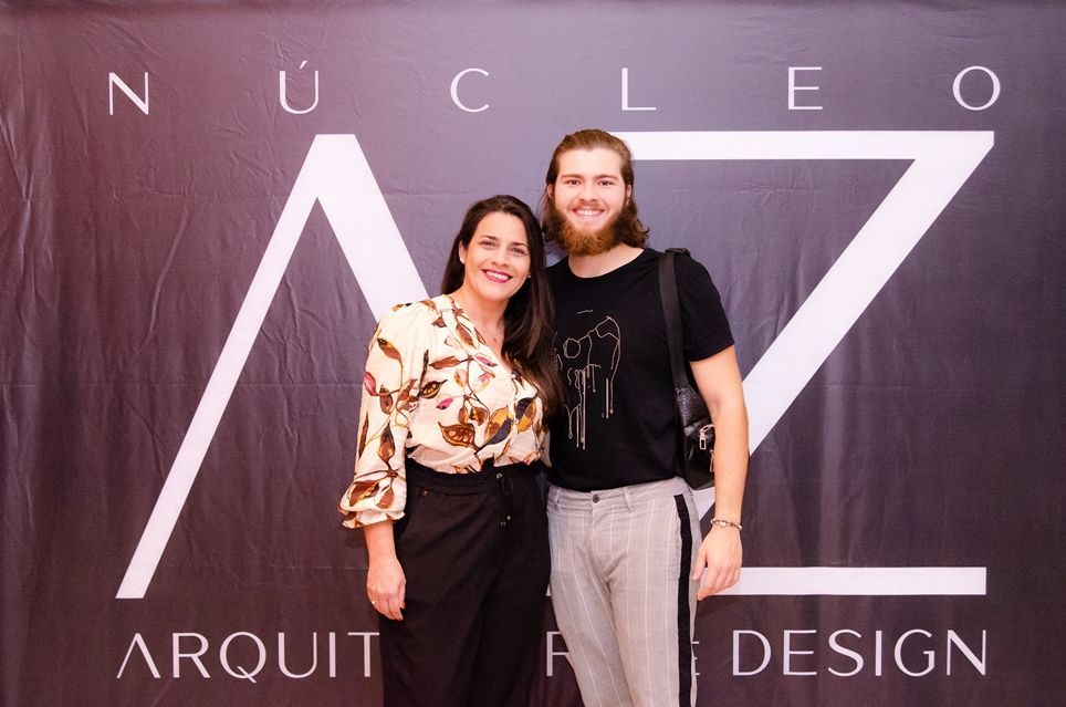 Um homem e uma mulher estão posando para uma foto em frente a uma placa que diz nucleo