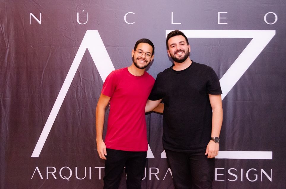 Dois homens estão posando para uma foto em frente a uma placa que diz nucleo
