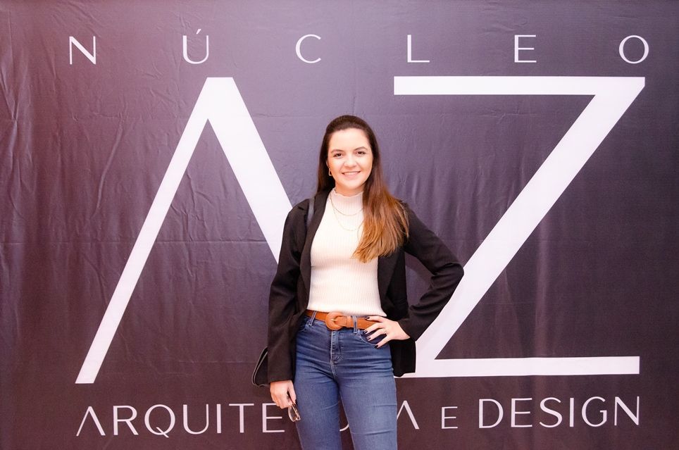 Uma mulher está parada em frente a uma placa que diz nucleo arquiteto e design