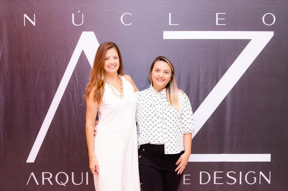 Duas mulheres posam para uma foto em frente a uma placa que diz arquie design