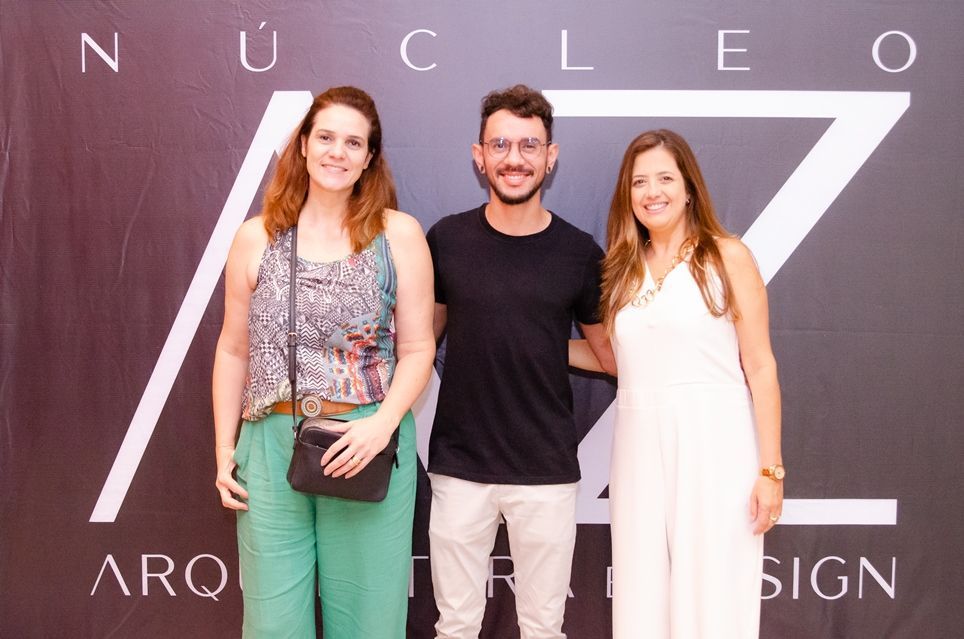 Três pessoas posando para uma foto em frente a uma placa que diz nucleo