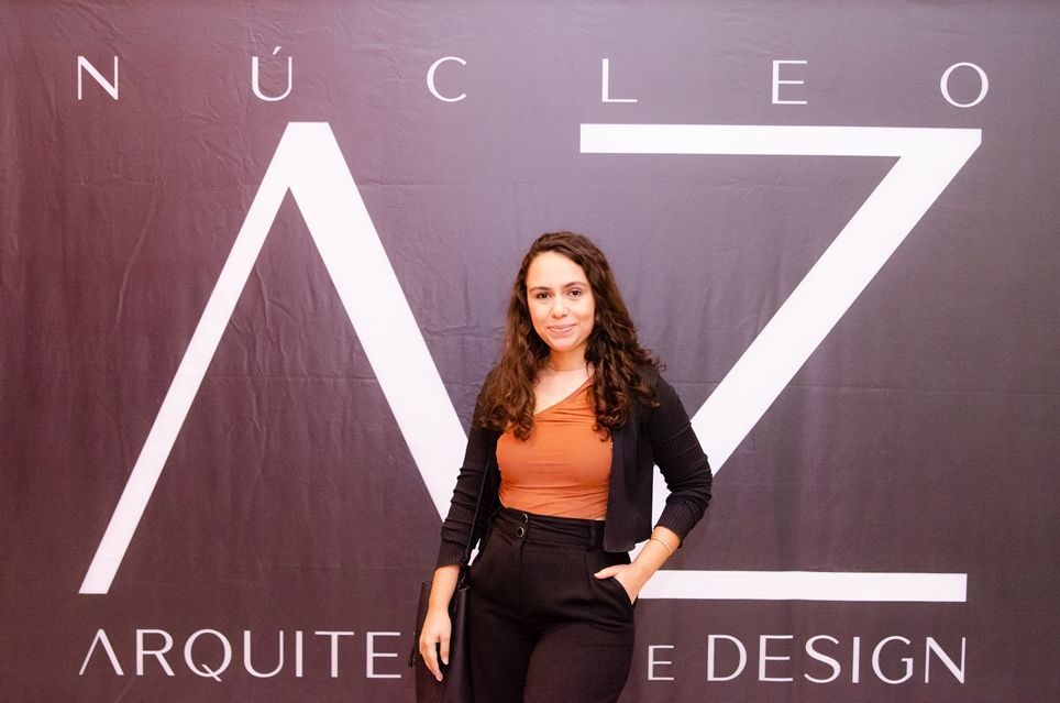 Uma mulher está parada em frente a uma placa que diz nucleo arquitete e design