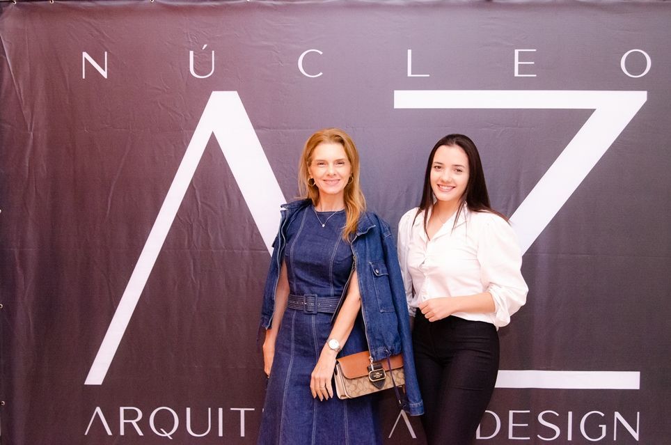 Duas mulheres estão de pé, uma ao lado da outra, em frente a uma placa.