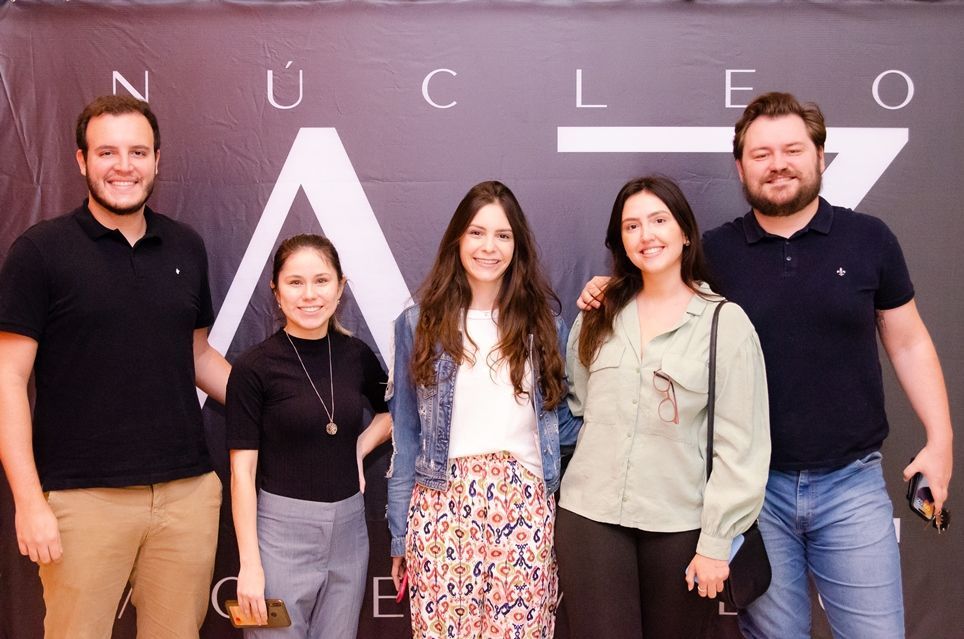 Um grupo de pessoas está posando para uma foto em frente a uma placa que diz nucleo.