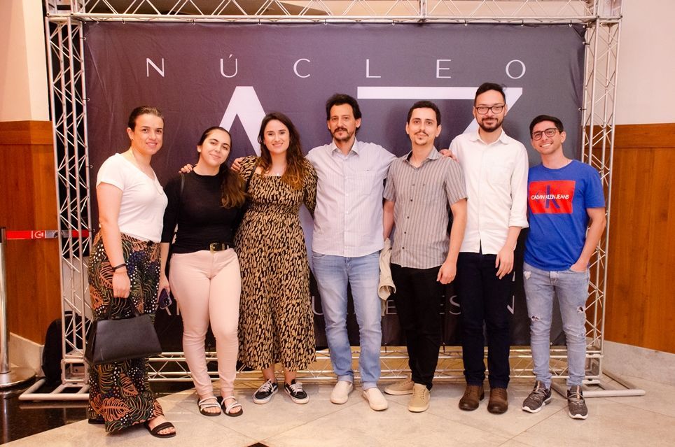Um grupo de pessoas está posando para uma foto em frente a uma placa que diz nucleo.