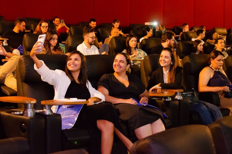 Um grupo de pessoas está sentado em um teatro tirando uma selfie.
